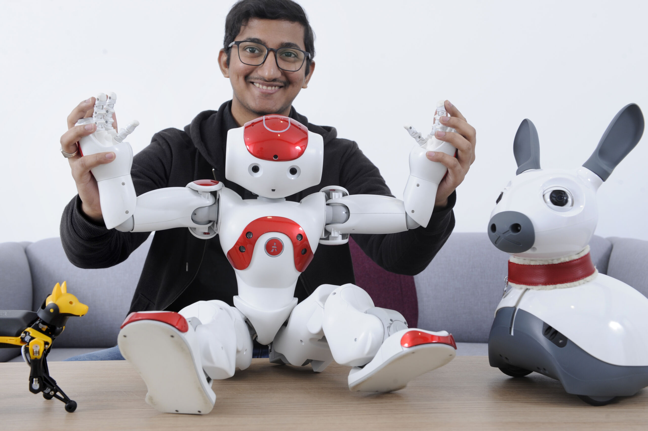 A man plays with a humanoid robot while a canine robot looks on